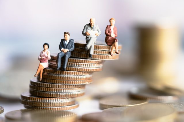 Kleine Figuren sitzen auf einem Stapel Münzen, der sehr wackelig aussieht. Symbolbild für die Inflation.