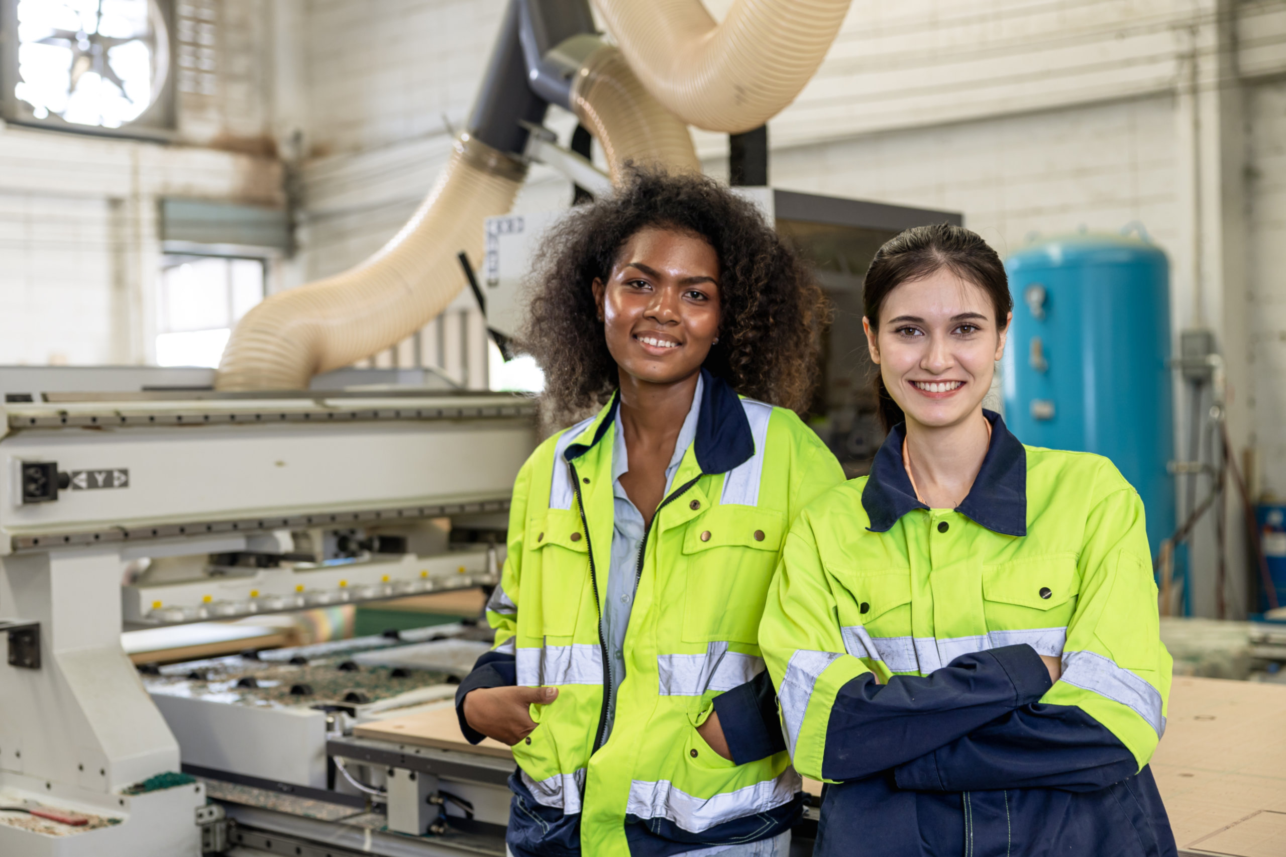 Zwei Arbeiterinnen mit Warnweste stehen in einer Fabrik. Der Kollektivvertrag in Österreich.