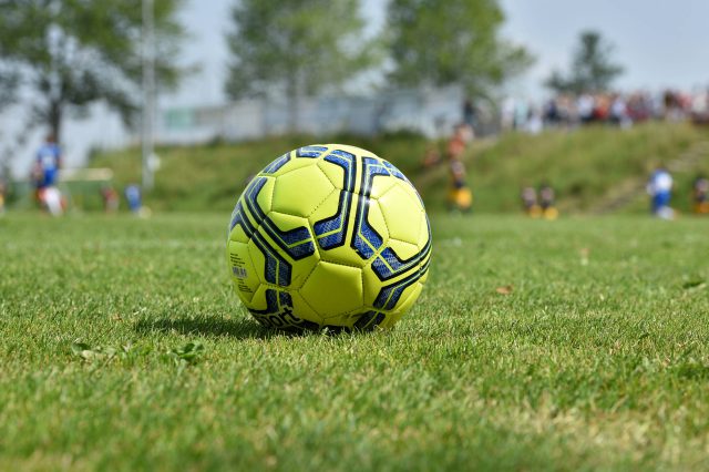 Ein gelber Fußball liegt auf einem Fußballplatz. Symbolbild für den Kollektivvertrag im Fußball in Österreich.