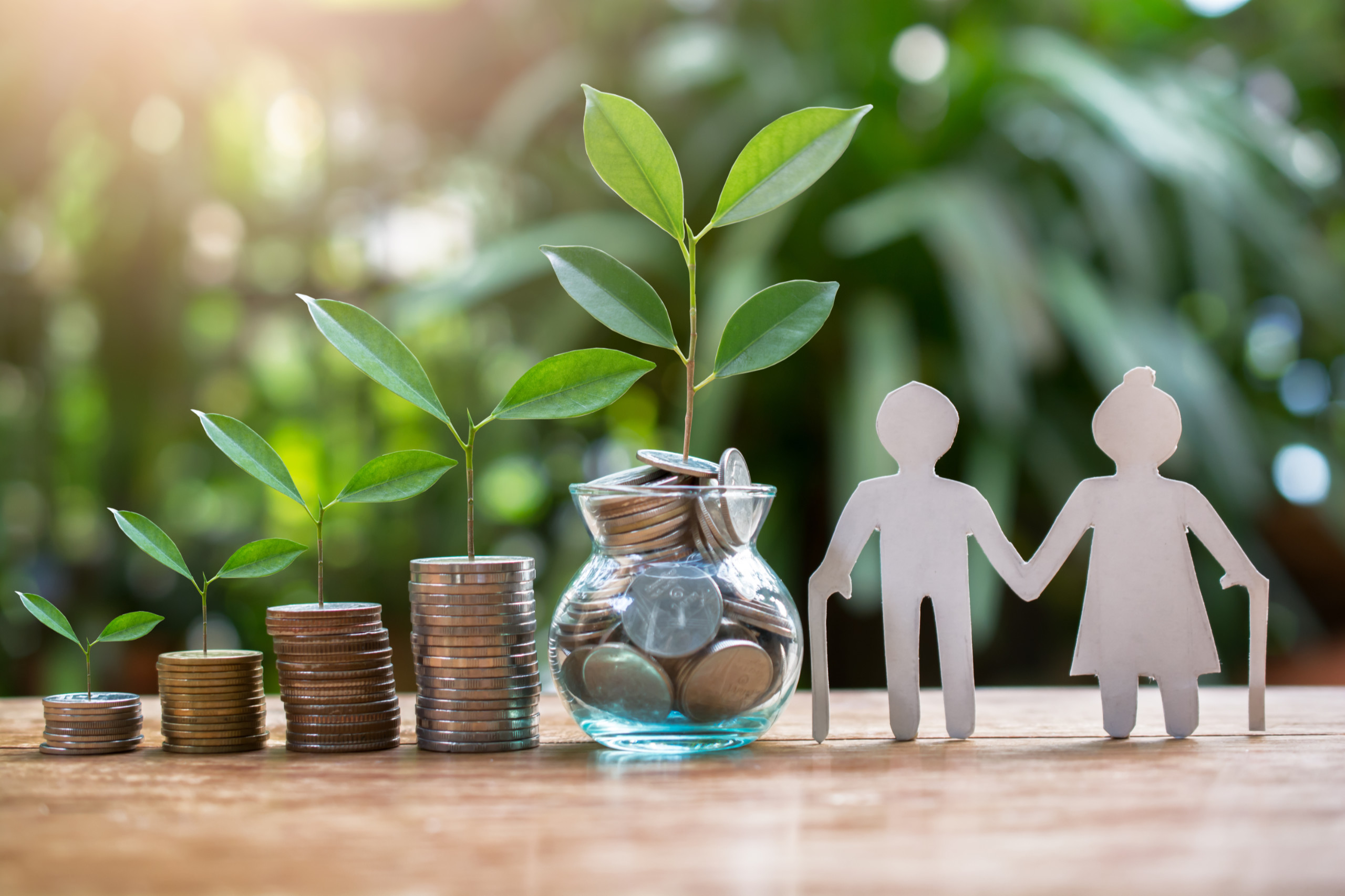 Ältere Personen, die als Figuren dargestellt sind, stehen neben ein paar Stapeln Geld, die immer größer werden. Symbolbild für die Pension in Österreich.