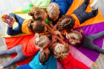 Kinder bilden bei einem Spiel im Kindergarten einen Kreis aus einer bunten Decke. Österreich muss die Kinderbetreuung ausbauen.