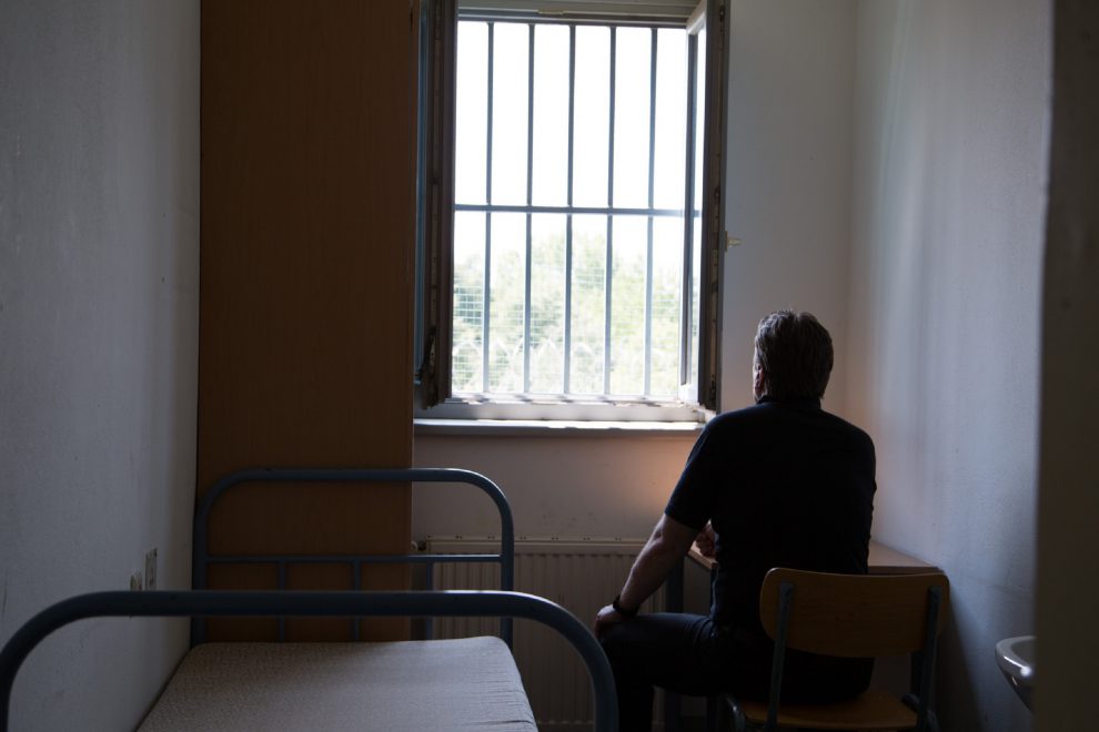 Ein Mann sitzt vor einem Fenster mit Gefängnisstäben. Symbolbild für Inhaftierte und Arbeit.