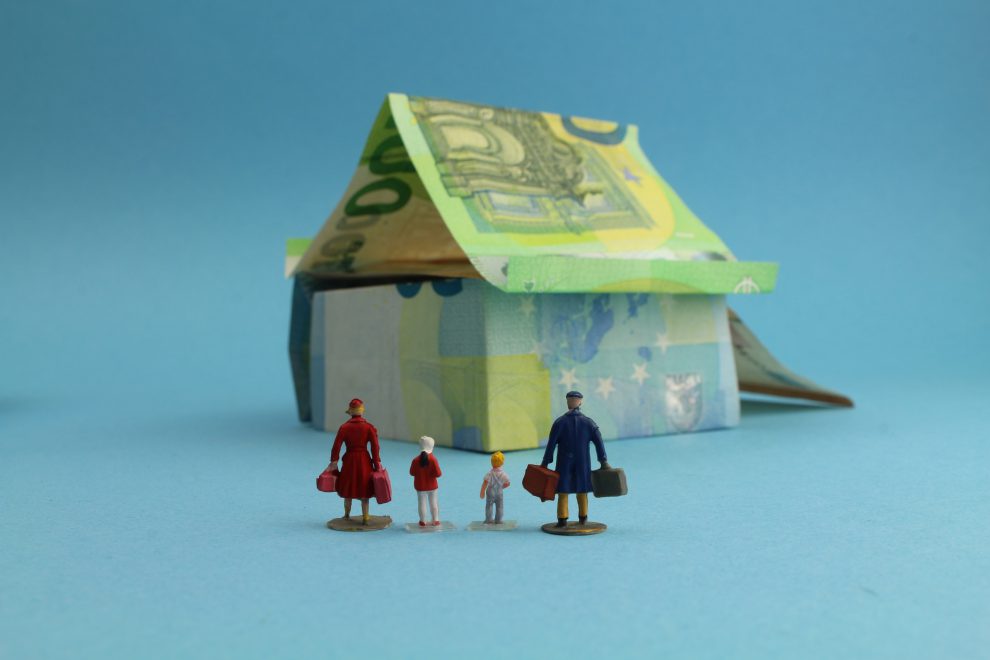 Haus aus Geldscheinen mit einer Familie im Vordergrund. Symbolbild für den gemeinnützigen Wohnbau.