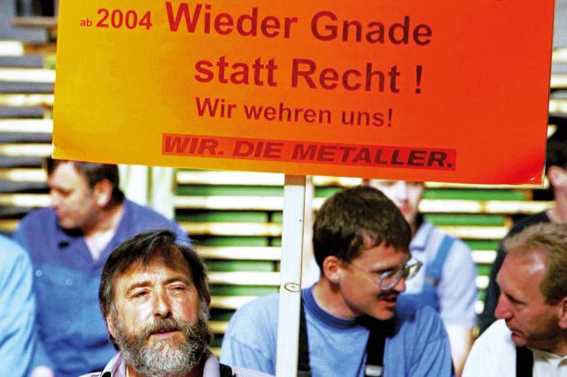 Metaller:innen halten bei einem Streik Schilder mit der Aufschrift "Wieder Gnade statt Recht. Wir wehren uns." hoch. Symbolbild für Angriffe auf den Sozialstaat.