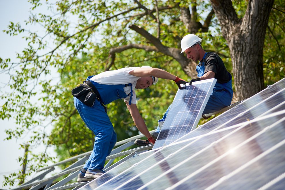 Männer stehen auf einer Photovoltaikanlage und arbeiten an ihr. Symbolbild für die Klimapolitik.