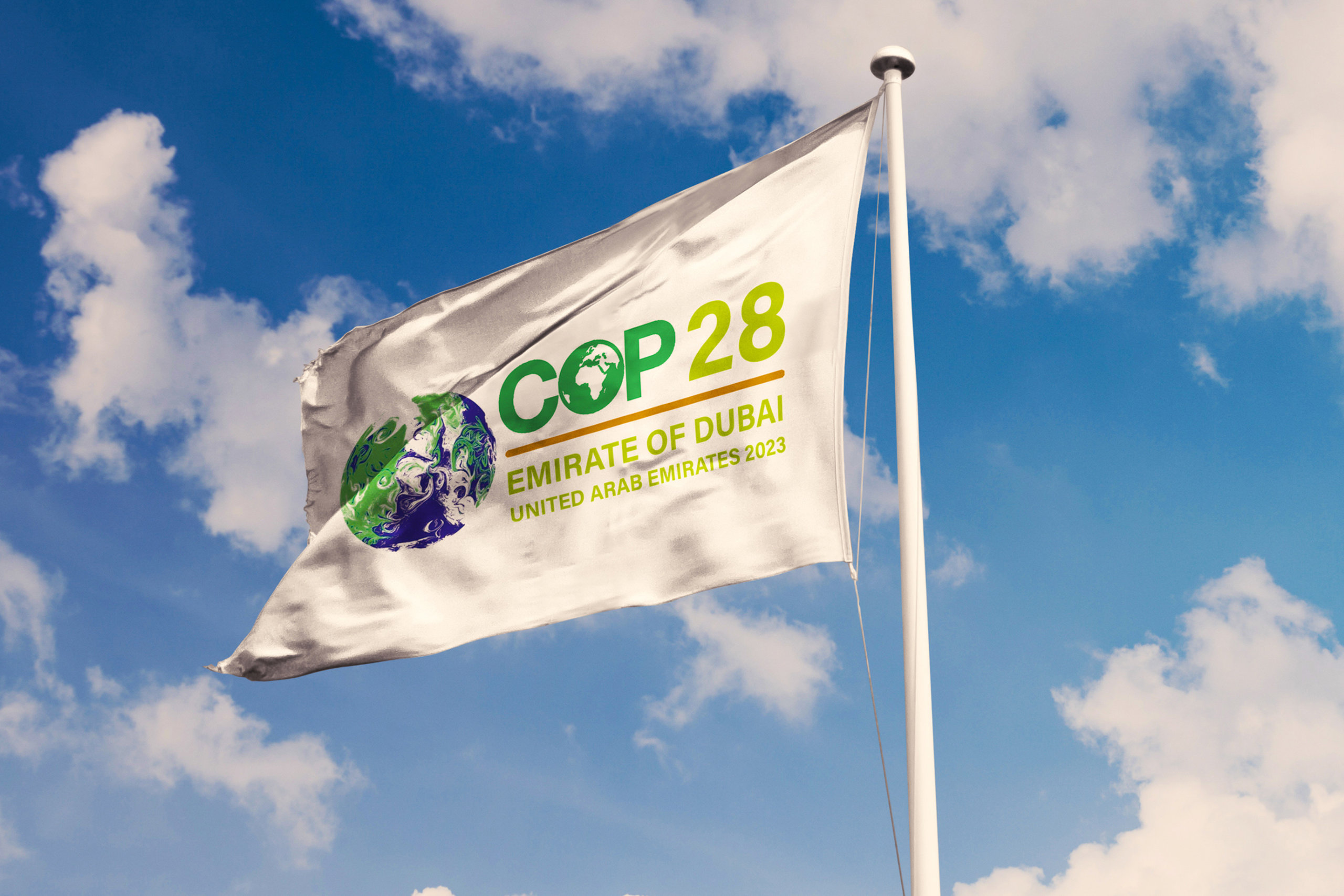 Eine Fahen der COP28 weht vor blauem Himmel im Wind.