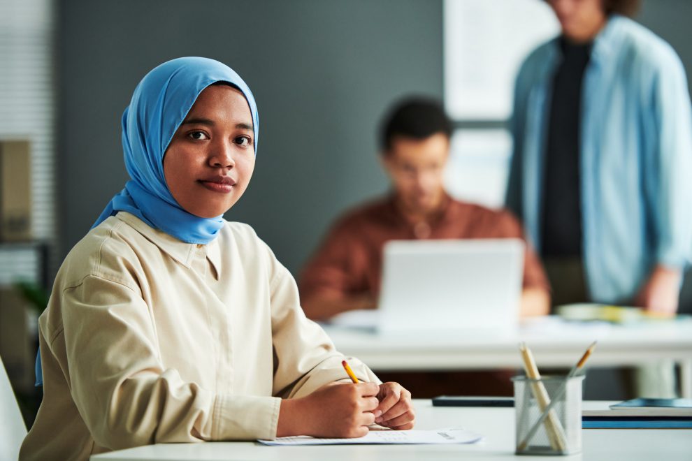 Eine Frau mit Hijab sitzt an einem Tisch und arbeitet. Symbolbild für Arbeitsmigration in Österreich.