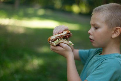 Kind isst Hamburger. Symbolbild für Sozialausgaben.