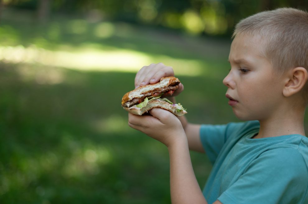 Kind isst Hamburger. Symbolbild für Sozialausgaben.