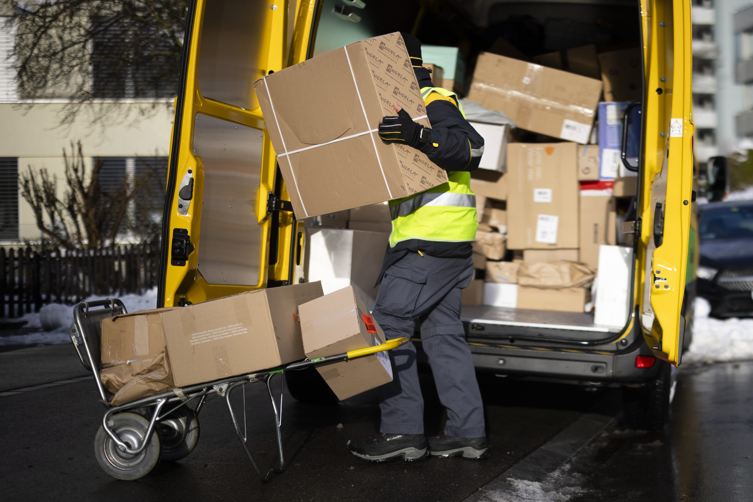 Ein Paketzusteller hievt ein Paket aus einem Auto. Symbolbild für die schlechten Arbeitsbedingungen der Paketzusteller:innen.