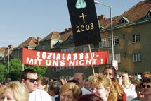 Eine Demo im Jahr 2003. Es ist eine Menschenmenge zu sehen, die Schilder mit der Aufschrift "Sozialabbau - mit uns nicht!" und "SVS, Kreuzzeichen, 2003" tragen. Symbolbild für den Leistungsabbau in der Sozialversicherung.