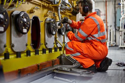 Ingenieur in einem orangenen Anzug arbeitet an einer Maschine. Symbolbild fürs Lohnnebenkosten senken.