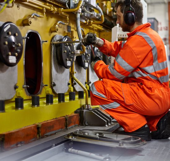 Ingenieur in einem orangenen Anzug arbeitet an einer Maschine. Symbolbild fürs Lohnnebenkosten senken.