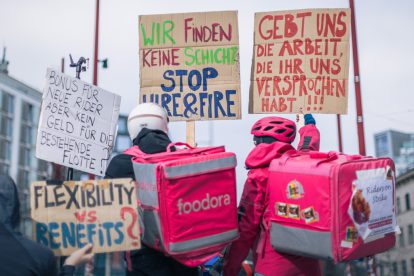 Foodora-Rider:innen demonstrieren auf der Mariahilfer. Auf den Schildern steht "Gebt uns die Arbeit, die ihr versprochen habt", "Wir finden keine Schichten. Stoppt Hire&Fire", "Flexibility vs. Benefits?", "Bonus für neue Rider, aber kein Geld für die bestehende Flotte".