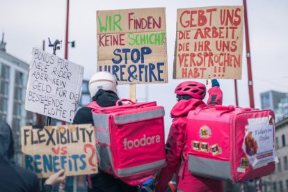 Foodora-Rider:innen demonstrieren auf der Mariahilfer. Auf den Schildern steht "Gebt uns die Arbeit, die ihr versprochen habt", "Wir finden keine Schichten. Stoppt Hire&Fire", "Flexibility vs. Benefits?", "Bonus für neue Rider, aber kein Geld für die bestehende Flotte".