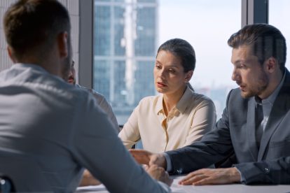 Eine Gruppe aus Menschen bestehend auf einer Frau und zwei Männern sitzen an einem Tisch und halten ein Meeting ab. Symbolbild für ein Wirtschaftsgespräch.