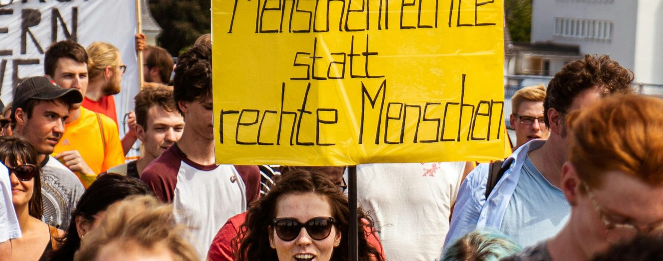 Eine Demonstration gegen Rechts. Eine Frau steht im Vordergrund und hält ein Schild mit der Aufschrift "Menschenrechte statt rechte Menschen". Daniela Ingruber erklärt im Interview den Erfolg rechter Populisten.