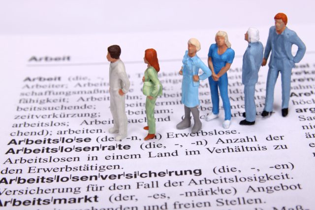 Modellbaufigürchen stehen auf der Seite des Dudens, auf der Arbeitslosigkeit erklärt wird.