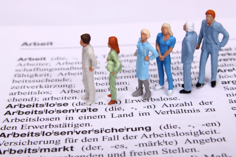 Modellbaufigürchen stehen auf der Seite des Dudens, auf der Arbeitslosigkeit erklärt wird.
