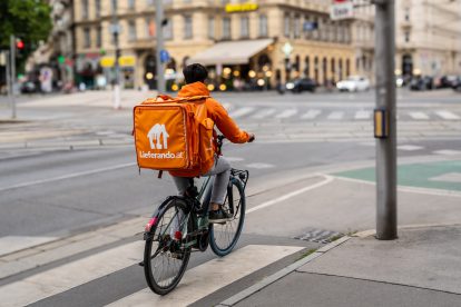 Ein Lieferando-Fahrradbote mit typischer orangefarbener Jacke wartet bis die Ampel grün wird