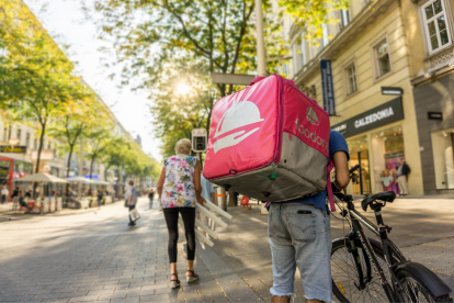 Ein Mann mit einem Foodora-Rucksack steht auf der Mariahilfer neben seinem Fahrrad.
