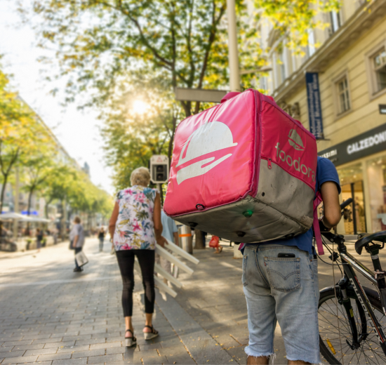 Ein Mann mit einem Foodora-Rucksack steht auf der Mariahilfer neben seinem Fahrrad.