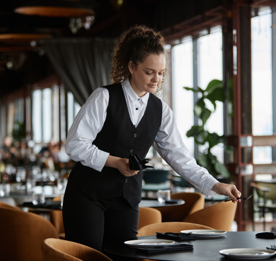 Eine Frau deckt in einem Restaurant einen Tisch. Symbolbild für das Arbeiten in der Gastro.