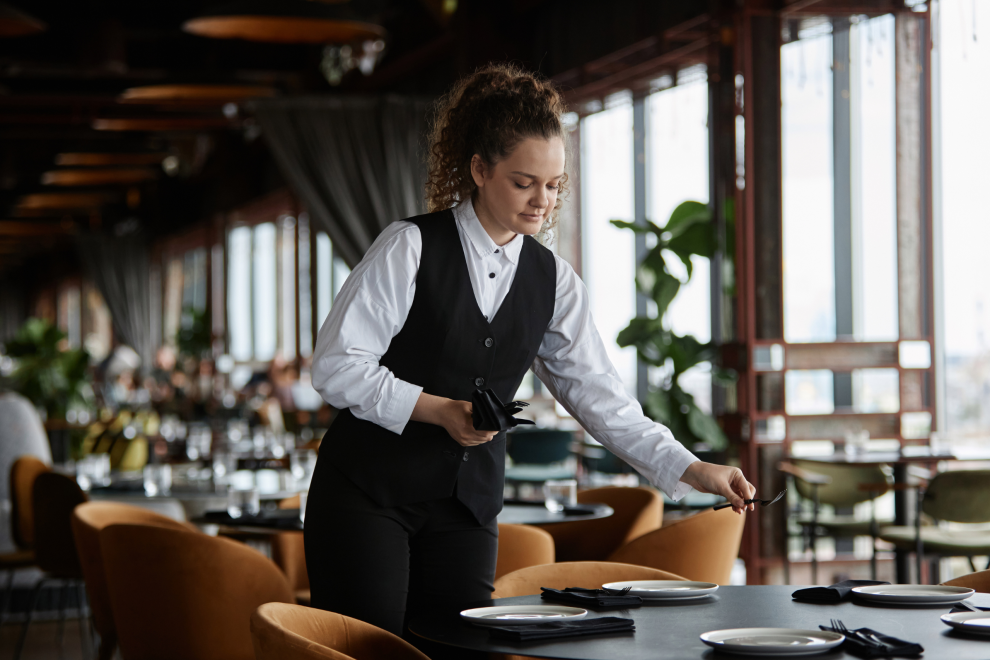 Eine Frau deckt in einem Restaurant einen Tisch. Symbolbild für das Arbeiten in der Gastro.