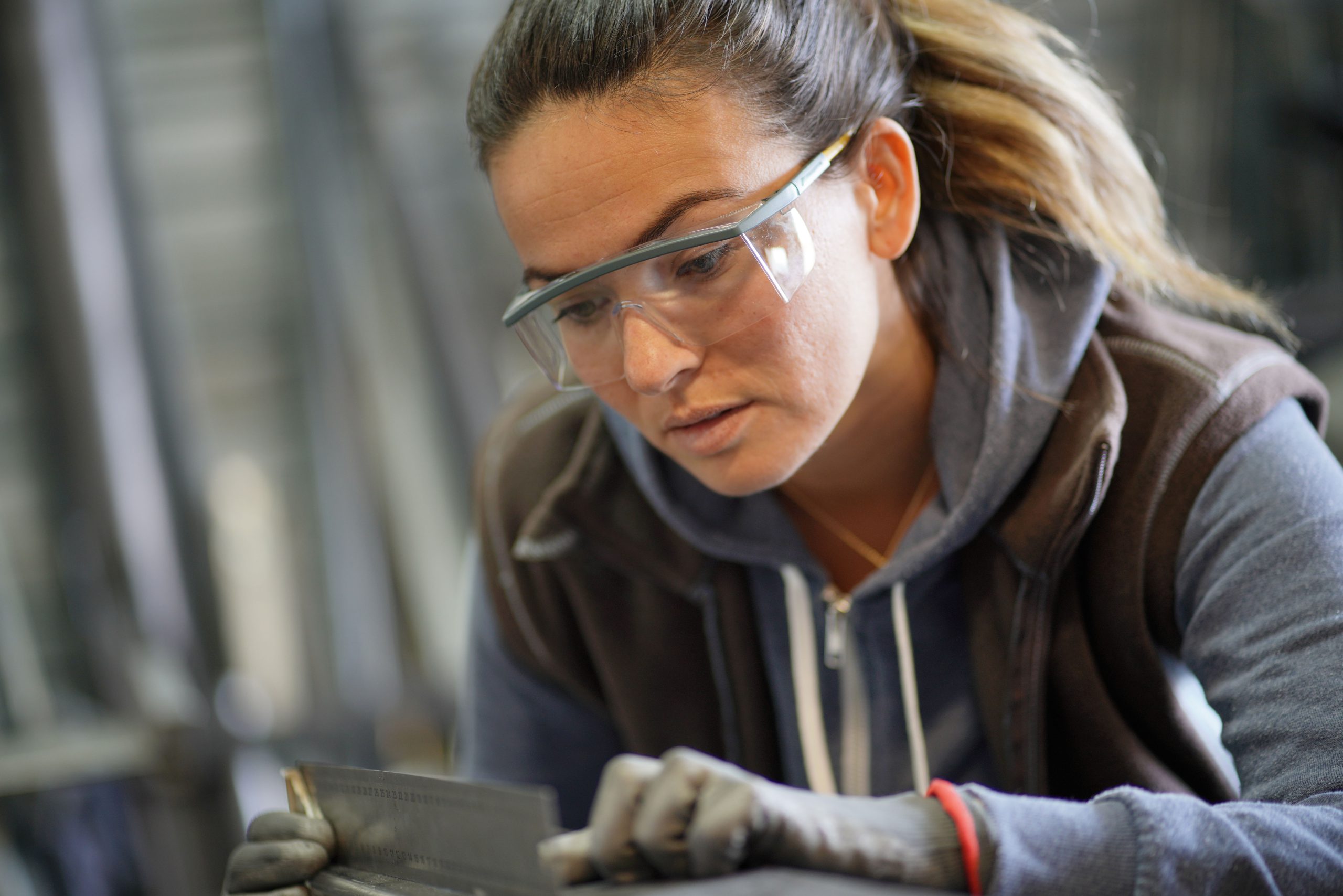 Eine Frau trägt eine Sicherheitsbrille und arbeitet mit Metall.