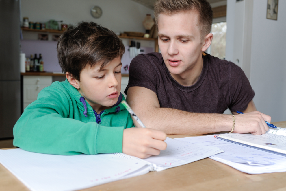 Ein Student gibt einem Kind Nachhilfeunterricht. Symbolbild für die hohen Kosten für Nachhilfe in Österreich. | © Adobe Stock/photophonie