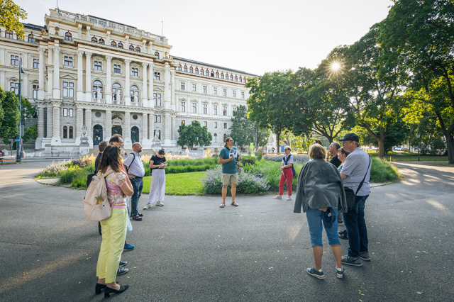 Vor dem Justizpalast steht eine Gruppe Menschen und hört einem Guide zu. Symobilbild für den Rundgang zu Arbeiter:innenbewegungen.