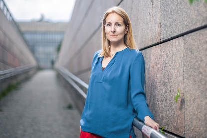 Julia Ehs ist Politologin und steht mit einem blauen Shirt vor einer Wand. Symbolbild für das Demokratieempfinden der Gesellschaft und wie sich dieses verändert.