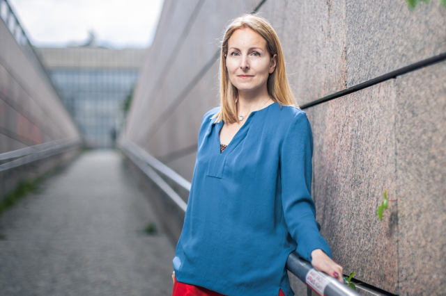 Julia Ehs ist Politologin und steht mit einem blauen Shirt vor einer Wand. Symbolbild für das Demokratieempfinden der Gesellschaft und wie sich dieses verändert.