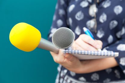 Eine Frau hält zwei Mikros und schreibt auf einem Block. Symbolbild für Qualitätsjournalismus fördern