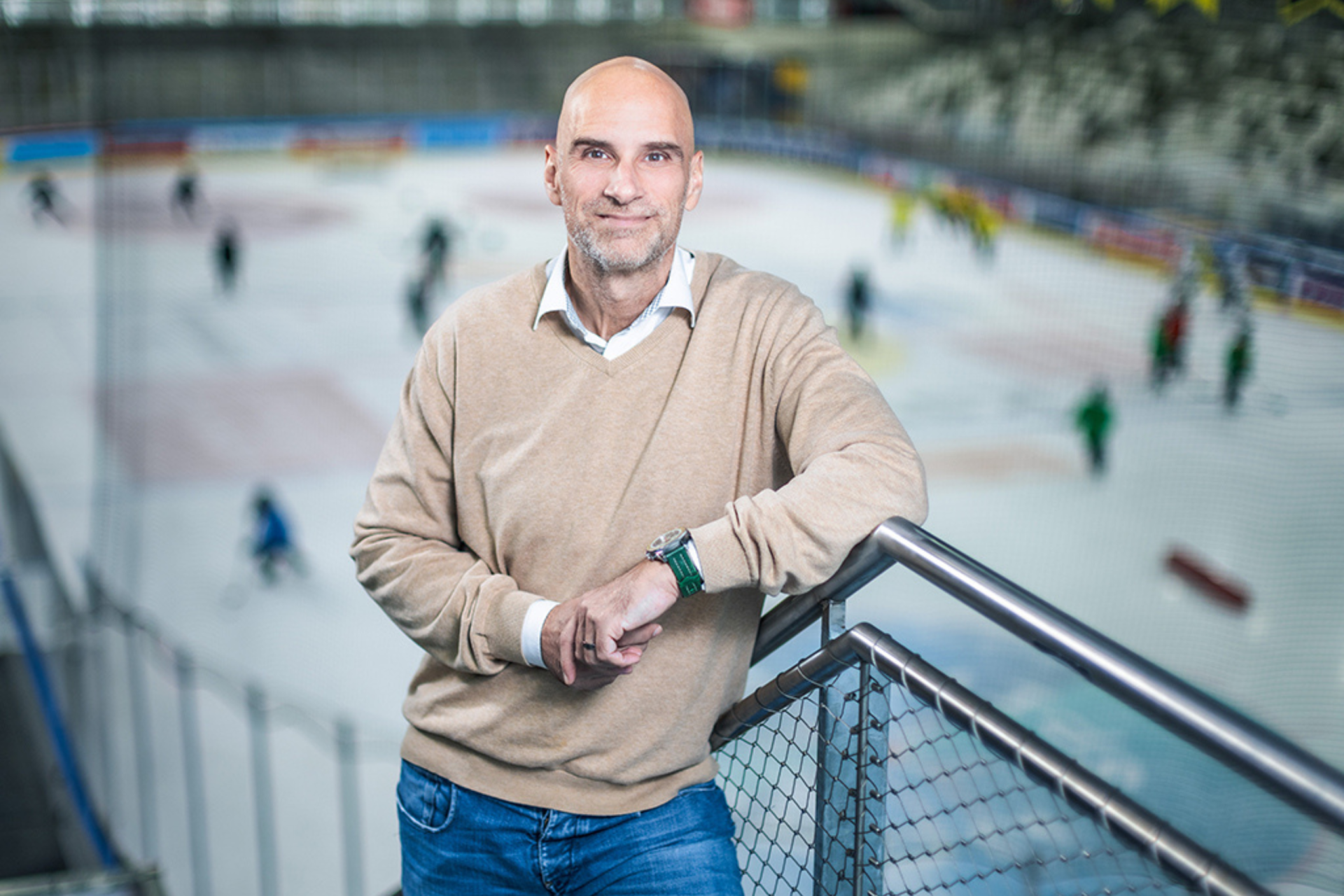 „Es gibt Vereine, die weniger zahlen als die Mindestlöhne in den Niedrigstbranchen“, sagt Alexander Tomanek, Jurist und ehemaliger Profisportler, über die Eishockey-Branche. Er steht vor dem Feld, hinter ihm sieht man die Spieler am Eis.