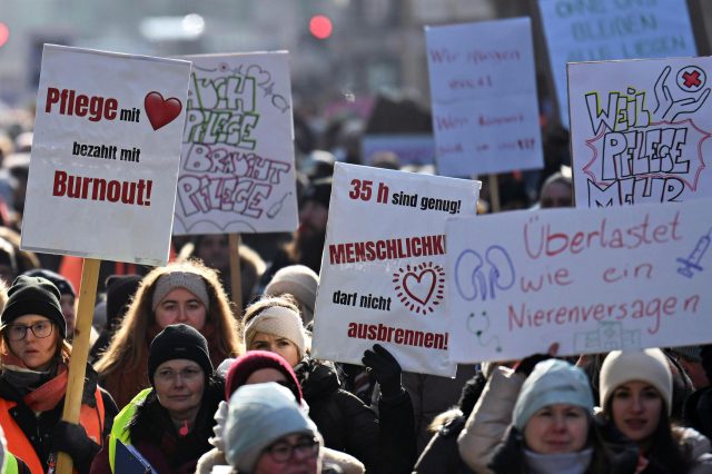 Menschen beim Streik mit Schildern in der Hand. Darauf steht "Pflege mit Herz bezahlt mit Burnout", "Auch Pflege braucht Pflege", 35h sind genug! Menschlichkeit darf nicht ausbrennen", "Überlastet wie ein Nierenversagen"