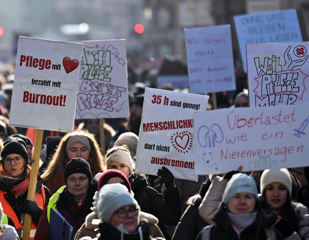 Menschen beim Streik mit Schildern in der Hand. Darauf steht "Pflege mit Herz bezahlt mit Burnout", "Auch Pflege braucht Pflege", 35h sind genug! Menschlichkeit darf nicht ausbrennen", "Überlastet wie ein Nierenversagen"