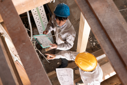 Zwei Bauarbeiter stehen auf der Baustelle und arbeiten mit einem Plan. Symbolbild: Häuser müssen sparsamer und klimafitter werden. Doch die Fachkräfte fehlen.