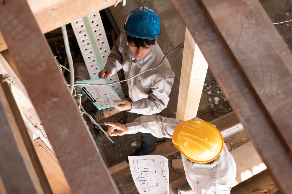 Zwei Bauarbeiter stehen auf der Baustelle und arbeiten mit einem Plan. Symbolbild: Häuser müssen sparsamer und klimafitter werden. Doch die Fachkräfte fehlen.