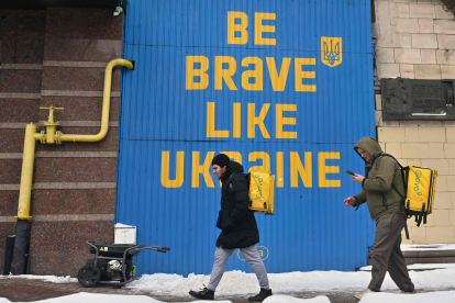 Lieferanten gehen während eines Stromausfalls im Zentrum von Kiew an einem laufenden Stromgenerator unter einem riesigen ukrainischen Kriegs-Slogan vorbei. Symbolbild: Die Rechte von Arbeitnehmer:innen in der Ukraine stehen zunehmend unter Druck. Die Gewerkschaften stehen vor großen Herausforderungen.