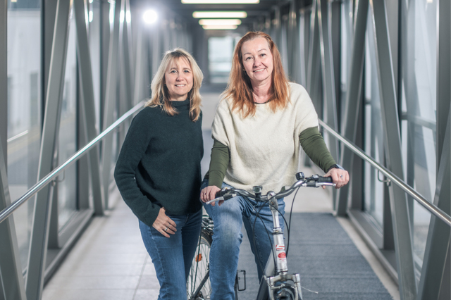 Die Betriebsrätinnen Ursula Sauer und Beatrix Wepner stehen um ein Fahrrad. Sie zeigen, was der Betriebsrat für mehr Klimaschutz tun kann.