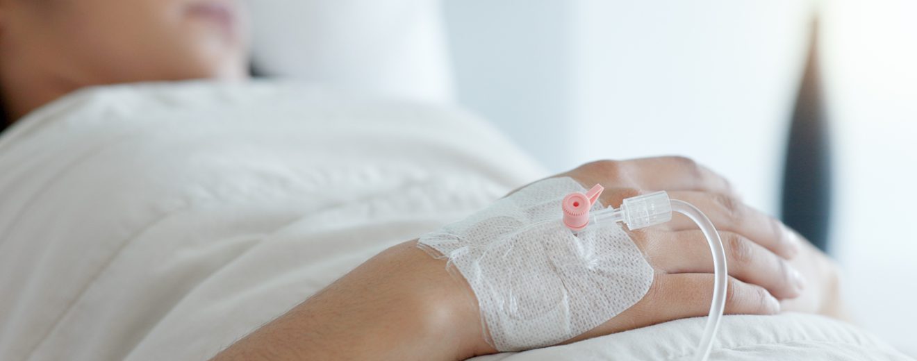 Eine Frau liegt in einem Krankenbett. In ihrer Hand steckt ein Zugang. Symbolbild für Frauen Gesundheit.
