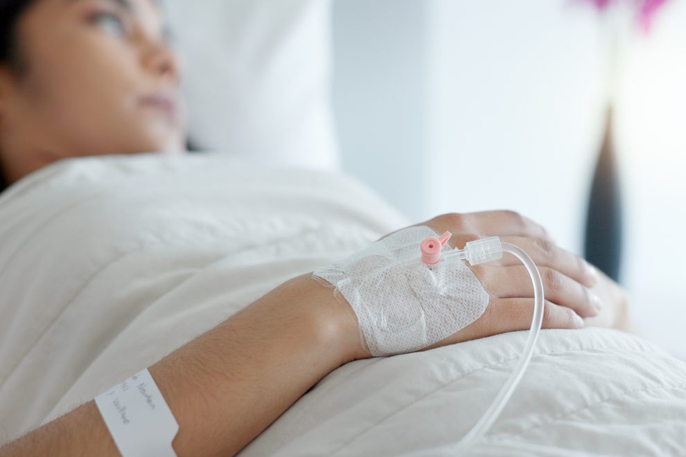 Eine Frau liegt in einem Krankenbett. In ihrer Hand steckt ein Zugang. Symbolbild für Frauen Gesundheit.