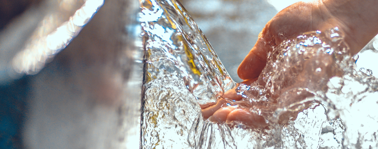 Eine Hand berührt einen Wasserstrahl. Symbolbild: Das Wasser könnte knapp werden. Aber wer verbraucht am meisten Wasser? Und wie verteilt man es im Ernstfall?