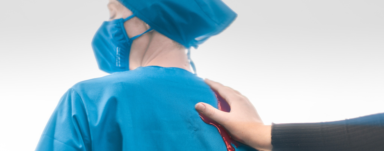 Eine Hand schmiert Blut auf die Uniform einer Pflegeperson. Symbolbild: ÖGB-Expert:innen Claudia Neumayer-Stickler und Julia Stroj möchten die Debatte um die Kassenfusion wieder ankurbeln.