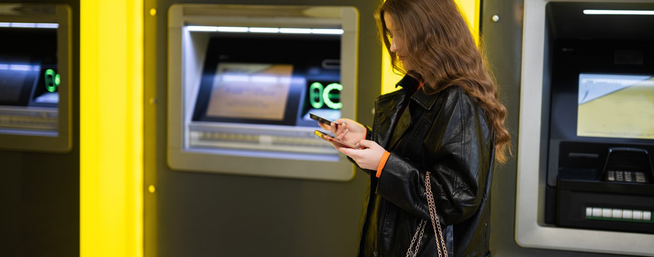 Eine Mädchen steht vor einem Bankomat. Symbolbild für Finanzbildung.