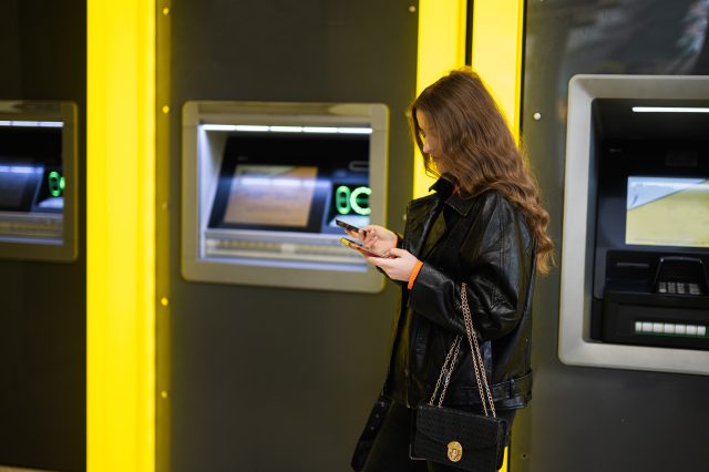 Eine Mädchen steht vor einem Bankomat. Symbolbild für Finanzbildung.