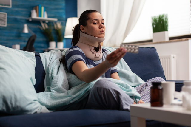 Eine Frau mit Halskrause und Medikamenten auf dem Sofa. Symbolbild für Krankenstände