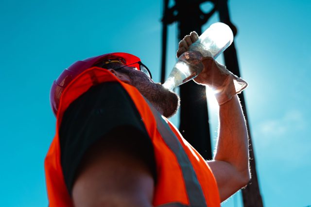 Ein Mann auf einer Baustelle trinkt Wasser. Es ist heiß. Symbbolbild: Klimakrise und Klimaschutzmaßnahmen.