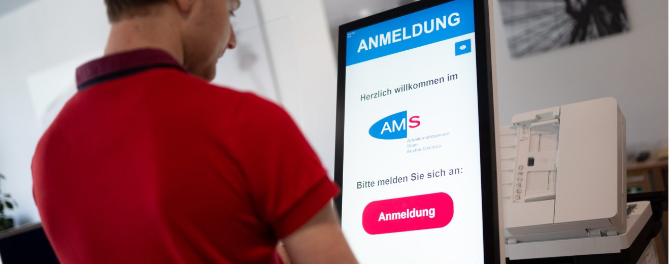 Ein Mann steht vor einem Bildschirm. Darauf ist "AMS. Anmeldung" zu lesen. Symbolbild für die Arbeitslosigkeit in Österreich.